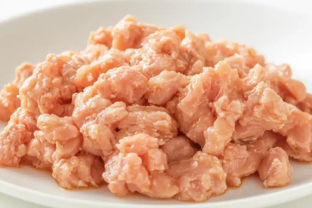 Can You Velvet Ground Chicken? 4 Close-up of raw velvet ground chicken on a white plate, showcasing its soft, silky texture. The chicken appears fresh and moist, ideal for stir-fries and dumplings.