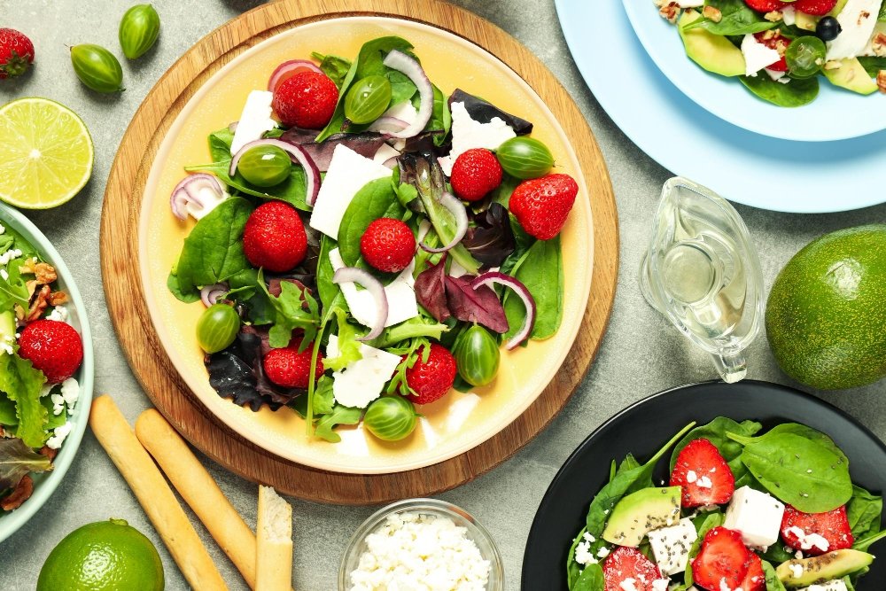 Top 10 Healthy Lunch Ideas for a Balanced Diet 3 Fresh and colorful mixed green salad with strawberries, avocado, feta cheese, and lime, displayed on vibrant plates with healthy toppings.