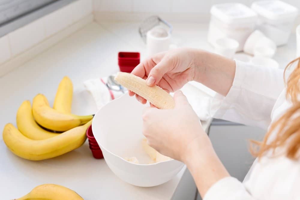 The Best Banana Bread Recipe: Simple and Quick 4 The Best Banana Bread Recipe: A person peeling a ripe banana into a mixing bowl in a bright kitchen, surrounded by fresh bananas and baking tools.