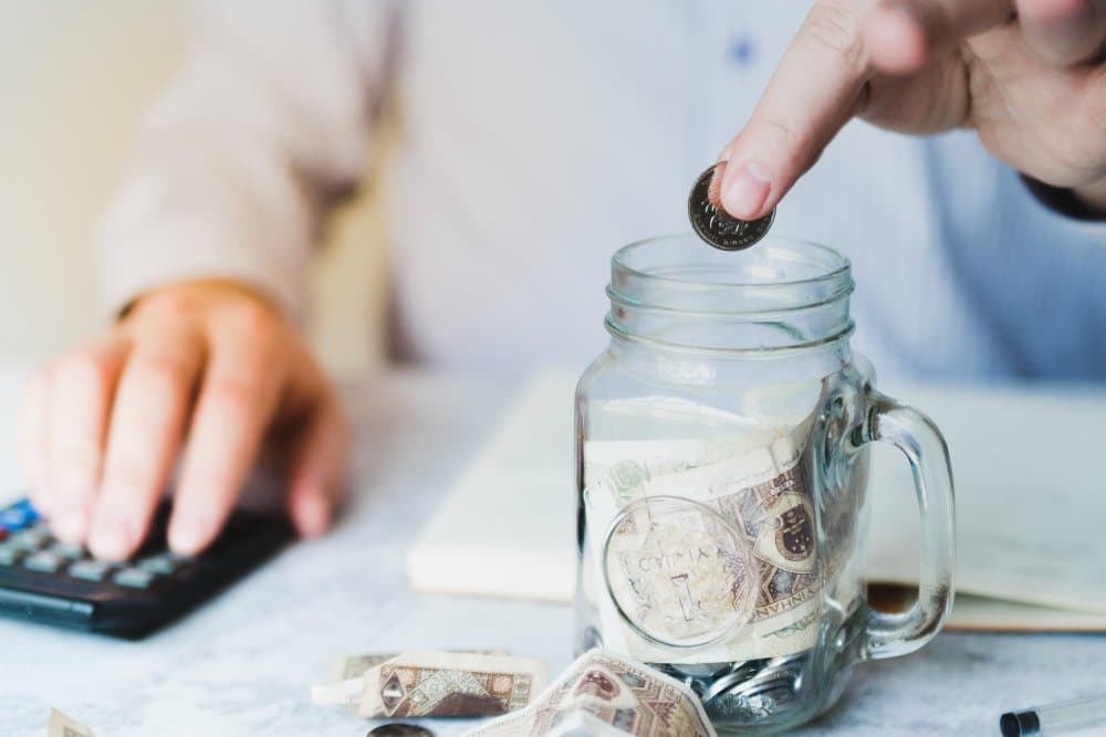 Easy Healthy Weeknight Dinners for Family 🍽️ 3 A person saving money in a glass jar while using a calculator, symbolizing budgeting and financial planning.