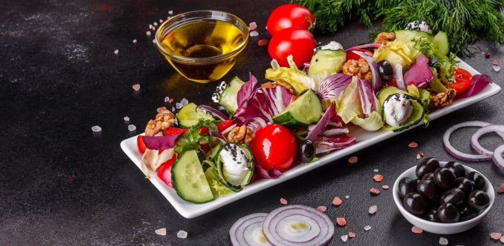 keto lunch recipes: Low-carb salad with fresh vegetables, cucumbers, cherry tomatoes, black olives, walnuts, and cream cheese on a white rectangular plate